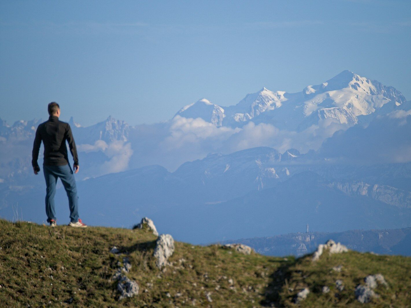 Man standing on a grassy hill overlooking mountains.