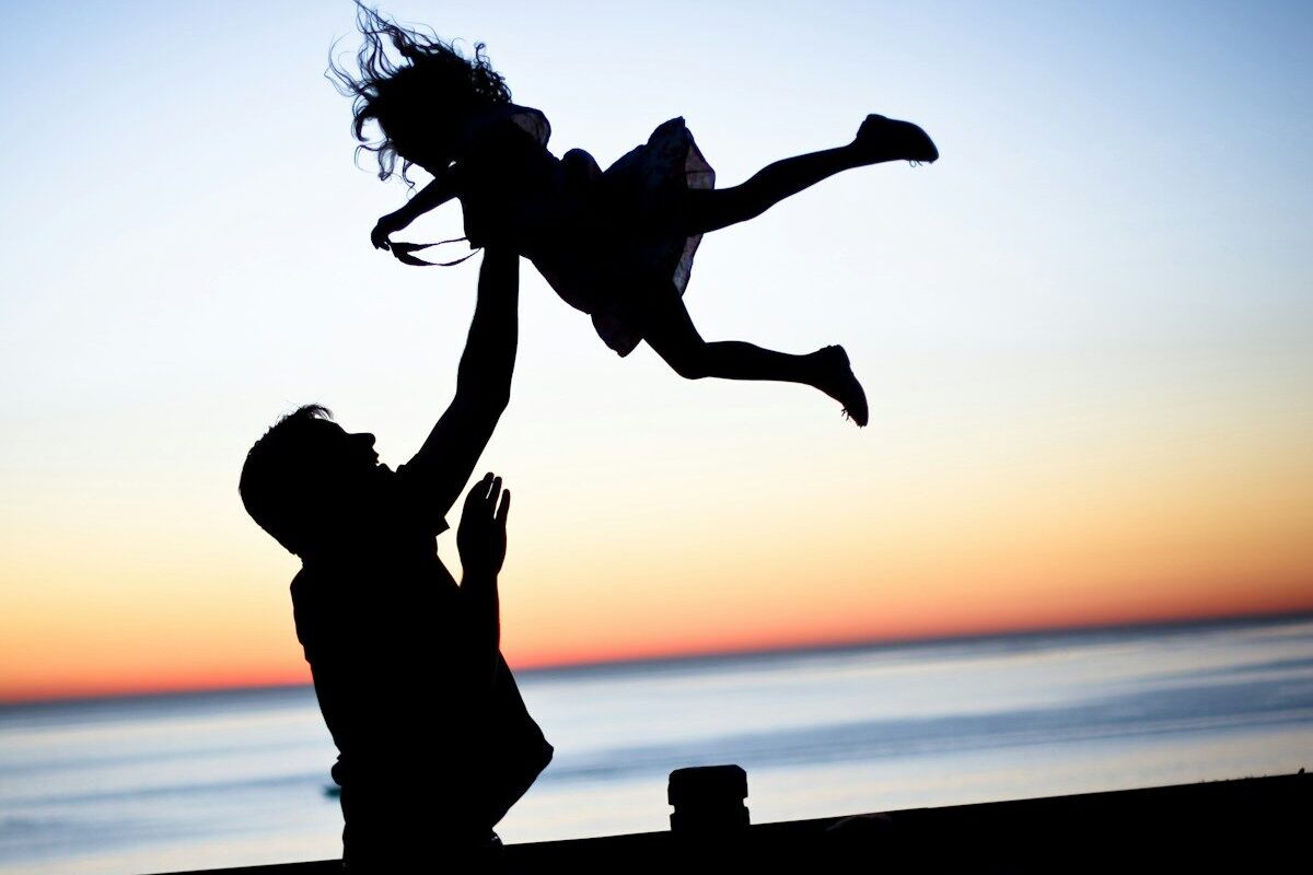 silhouette of man throwing girl in air